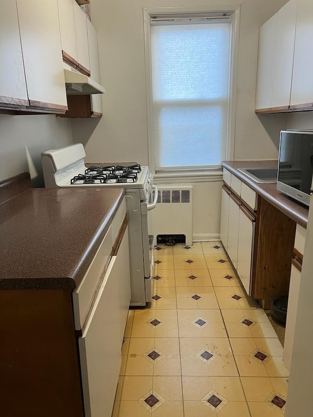 kitchen featuring white cabinets, gas range, radiator, and light tile patterned flooring