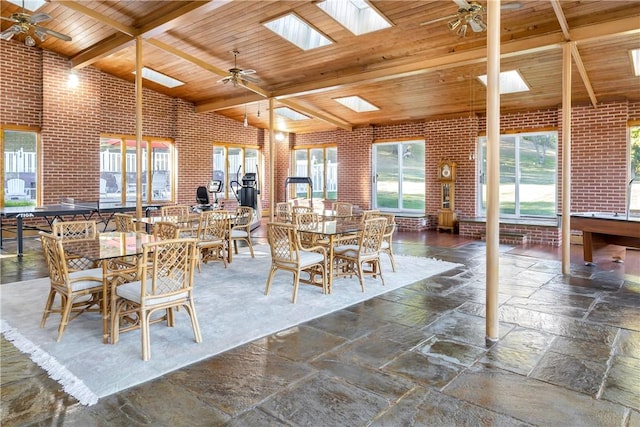 dining space with high vaulted ceiling, a skylight, ceiling fan, beam ceiling, and brick wall