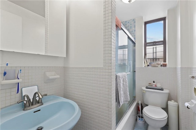 full bathroom featuring sink, bath / shower combo with glass door, tile walls, and toilet