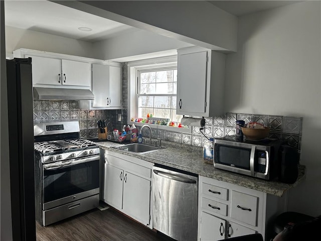 kitchen with under cabinet range hood, a sink, white cabinetry, appliances with stainless steel finishes, and decorative backsplash