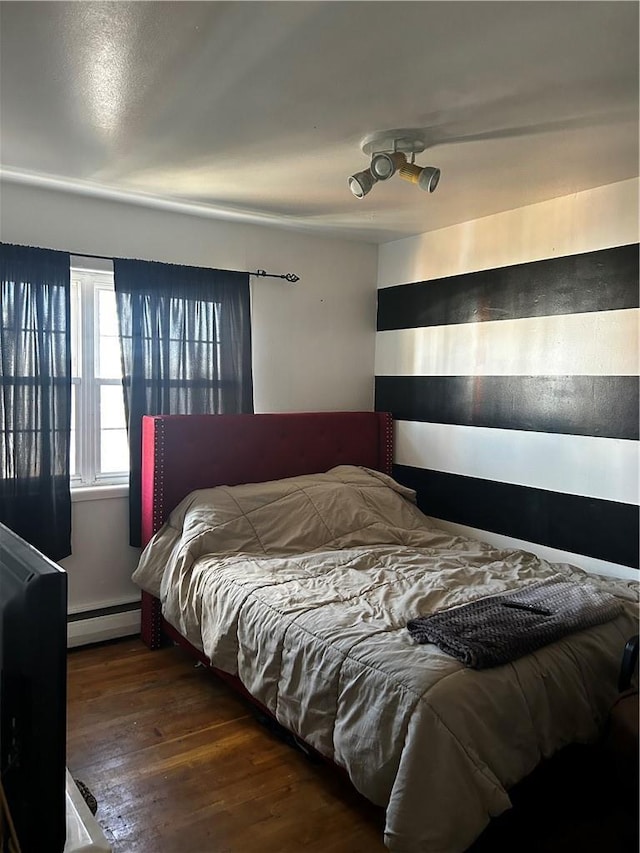 bedroom with a baseboard heating unit and wood finished floors