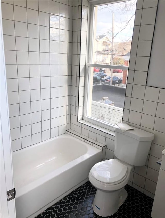 bathroom featuring tile patterned flooring, toilet, a wealth of natural light, and tile walls