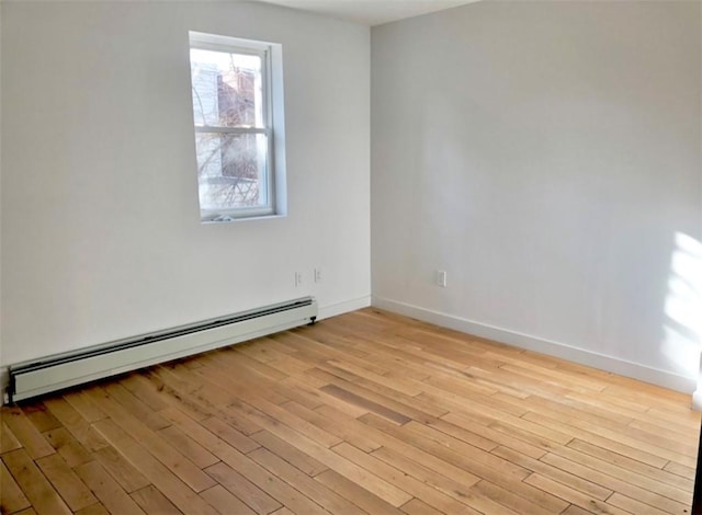 spare room featuring baseboard heating and light hardwood / wood-style floors