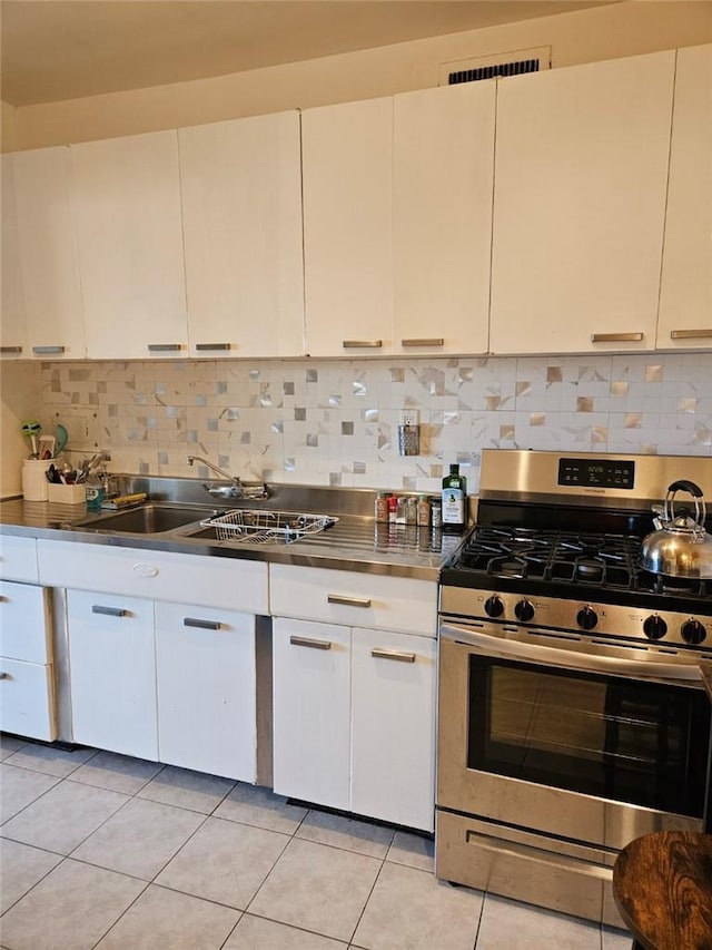 kitchen featuring sink, light tile patterned floors, decorative backsplash, white cabinets, and stainless steel range with gas stovetop