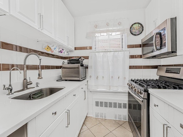 kitchen featuring radiator, sink, light tile patterned flooring, white cabinetry, and stainless steel appliances