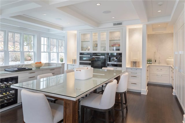 kitchen featuring beverage cooler, a kitchen island, dark hardwood / wood-style flooring, a breakfast bar, and white cabinets