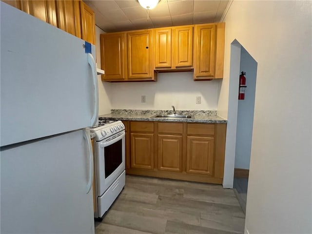 kitchen with white appliances, light hardwood / wood-style floors, light stone counters, and sink