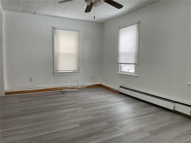 unfurnished room with a baseboard radiator, light hardwood / wood-style flooring, ceiling fan, and wooden walls