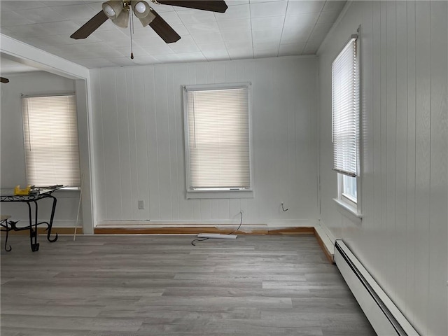 empty room featuring light wood-type flooring, baseboard heating, wood walls, and ceiling fan