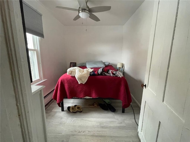 bedroom with light hardwood / wood-style floors, baseboard heating, and ceiling fan