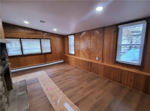 spare room featuring a healthy amount of sunlight, baseboard heating, wood-type flooring, lofted ceiling, and wooden walls