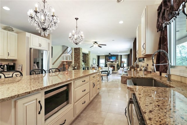 kitchen featuring ceiling fan with notable chandelier, sink, decorative light fixtures, light stone counters, and stainless steel appliances