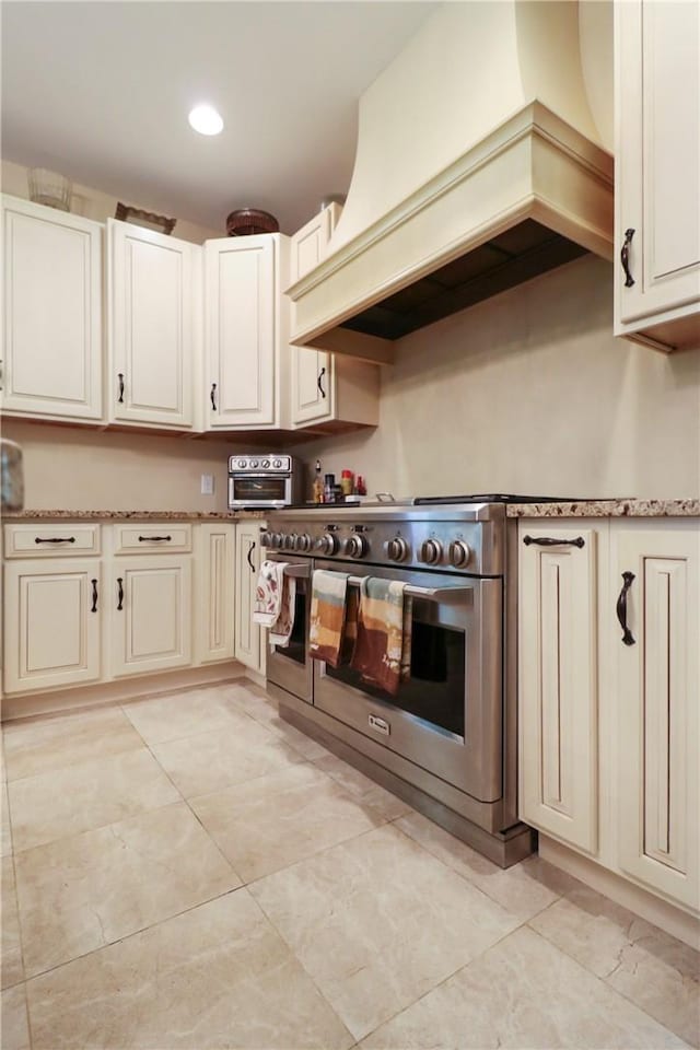 kitchen featuring range with two ovens, premium range hood, and cream cabinets