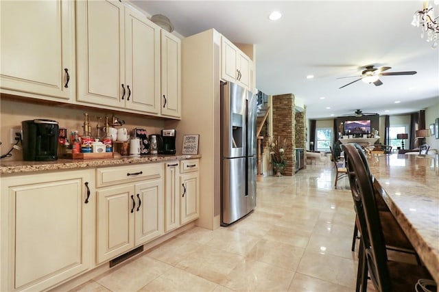 kitchen with ceiling fan, light stone countertops, cream cabinetry, light tile patterned flooring, and stainless steel fridge with ice dispenser