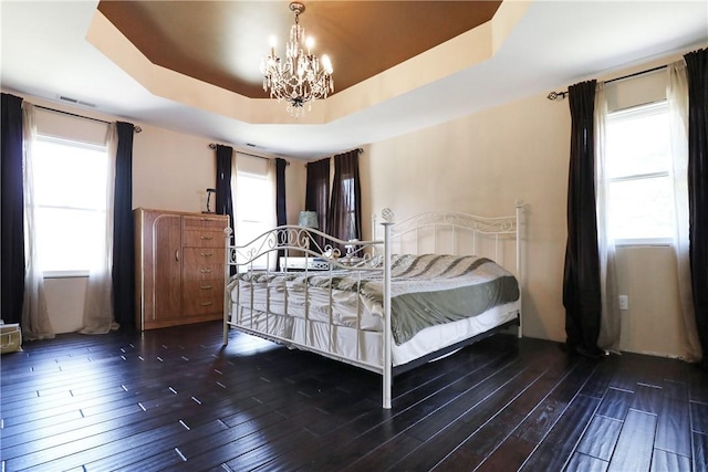 bedroom featuring dark hardwood / wood-style floors, a tray ceiling, and multiple windows