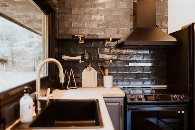 kitchen featuring sink, wall chimney range hood, and stainless steel range with electric cooktop