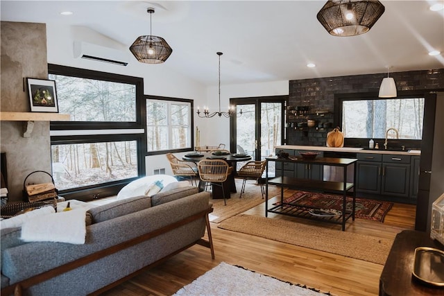 living room featuring hardwood / wood-style floors, lofted ceiling, an AC wall unit, sink, and a notable chandelier