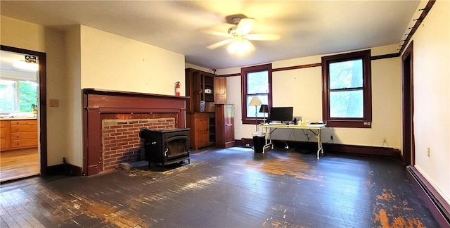 unfurnished office with a wood stove, ceiling fan, dark wood-type flooring, and a baseboard heating unit