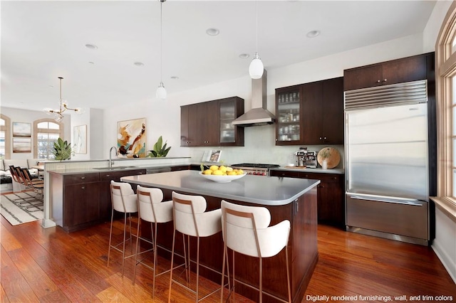 kitchen featuring dark brown cabinetry, wall chimney range hood, dark wood-type flooring, and appliances with stainless steel finishes