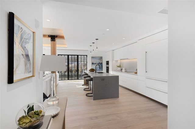 kitchen with sink, white cabinetry, a kitchen breakfast bar, pendant lighting, and a kitchen island with sink