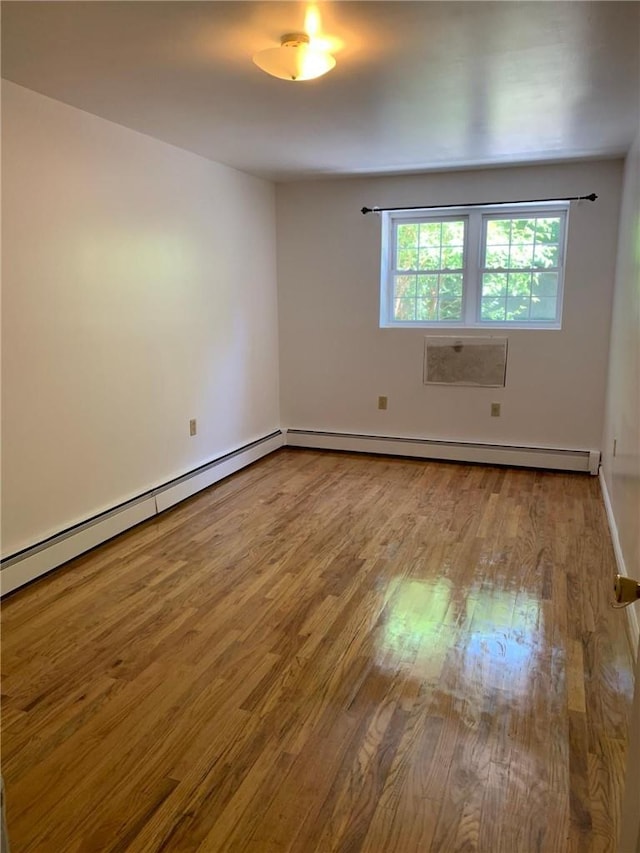 spare room featuring baseboard heating and wood-type flooring