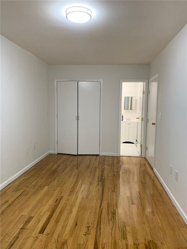 unfurnished bedroom featuring a closet, light wood-type flooring, and ensuite bath