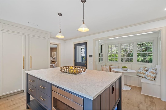 kitchen with light wood-type flooring, breakfast area, pendant lighting, a kitchen island, and stainless steel microwave