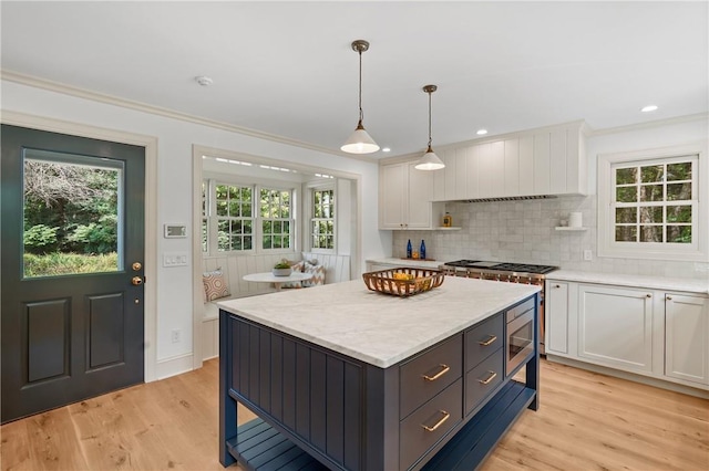 kitchen featuring stainless steel microwave, a kitchen island, decorative light fixtures, light hardwood / wood-style floors, and white cabinetry