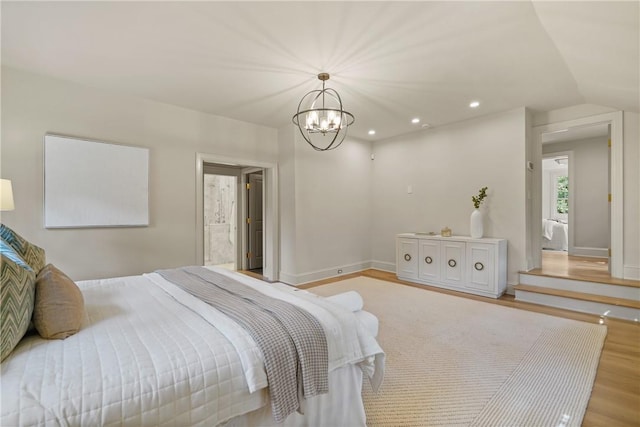 bedroom with vaulted ceiling, light hardwood / wood-style flooring, a notable chandelier, and connected bathroom