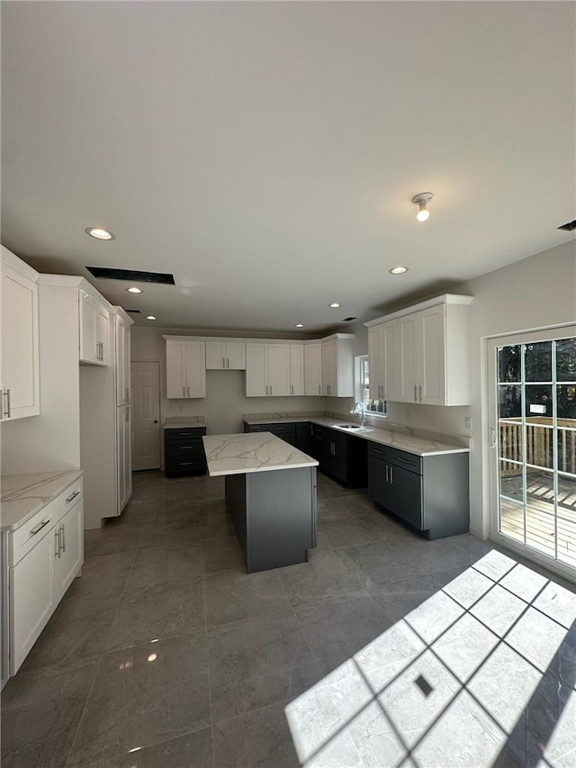 kitchen featuring a kitchen island, light stone countertops, white cabinetry, and sink