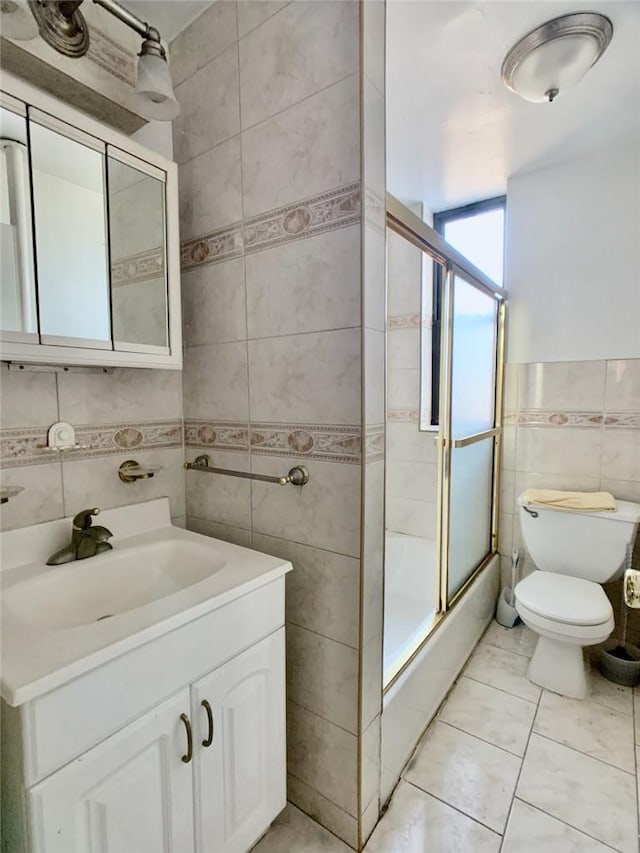 full bathroom featuring combined bath / shower with glass door, vanity, toilet, and tile walls