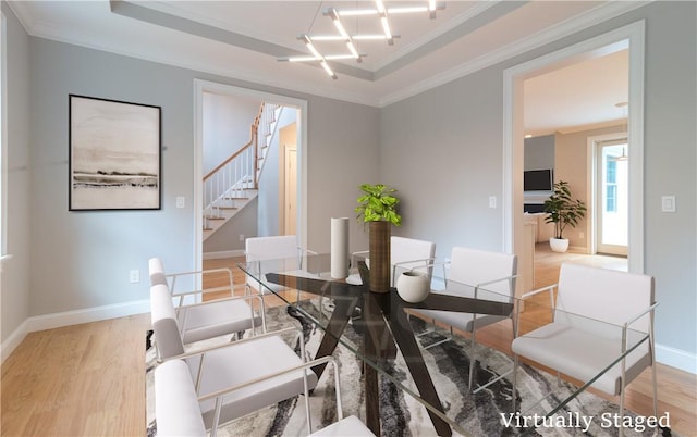 dining room with a tray ceiling, an inviting chandelier, light wood-type flooring, and ornamental molding