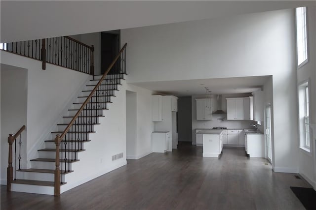 unfurnished living room featuring a towering ceiling, dark wood-type flooring, and sink