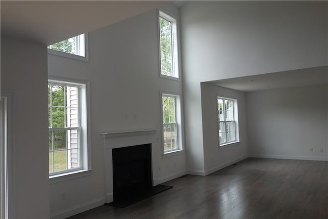 unfurnished living room featuring a high ceiling, dark wood-type flooring, and a healthy amount of sunlight