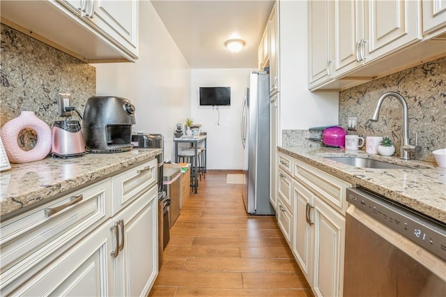 kitchen featuring decorative backsplash, appliances with stainless steel finishes, light stone countertops, sink, and light hardwood / wood-style flooring