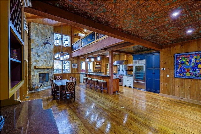 dining room featuring a fireplace, beam ceiling, hardwood / wood-style flooring, and wood walls