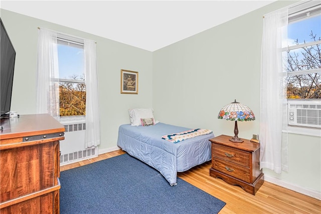 bedroom with radiator heating unit, cooling unit, and light hardwood / wood-style flooring