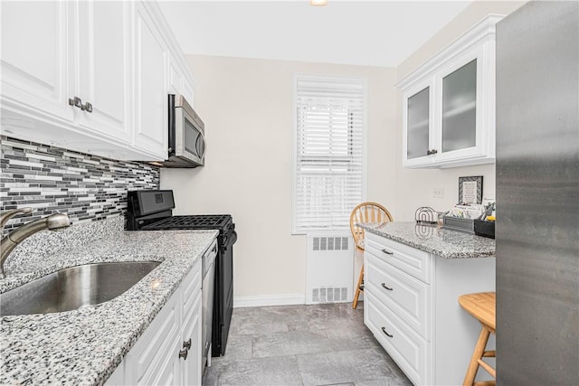 kitchen featuring radiator, sink, black range with electric cooktop, light stone counters, and white cabinetry