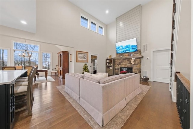 living room featuring hardwood / wood-style flooring, a notable chandelier, a stone fireplace, and a towering ceiling