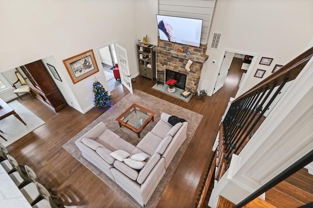 living room with a stone fireplace, dark hardwood / wood-style flooring, and a towering ceiling