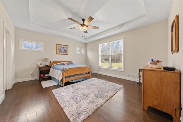 bedroom with dark hardwood / wood-style floors, ceiling fan, and a tray ceiling