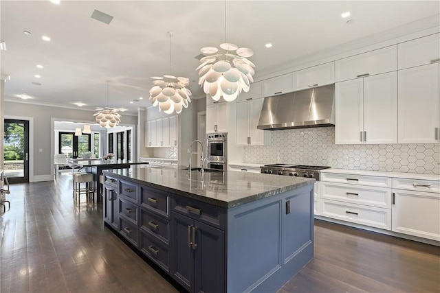 kitchen featuring dark hardwood / wood-style flooring, crown molding, decorative light fixtures, a center island with sink, and white cabinets