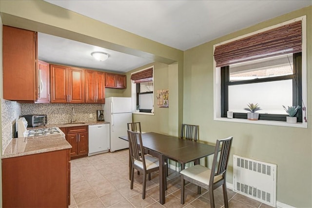 kitchen with light stone countertops, radiator heating unit, sink, tasteful backsplash, and white appliances