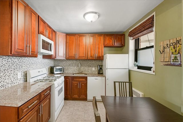 kitchen with white appliances, sink, light stone countertops, light tile patterned floors, and tasteful backsplash