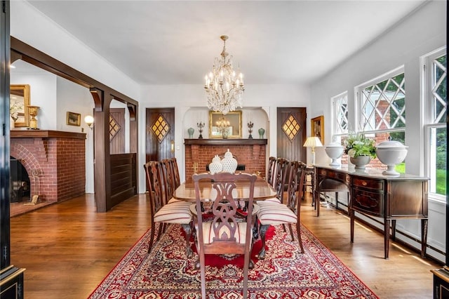 dining room with a brick fireplace, a chandelier, a baseboard heating unit, and hardwood / wood-style flooring