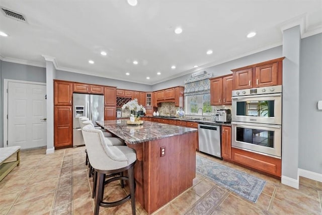 kitchen featuring decorative backsplash, appliances with stainless steel finishes, dark stone counters, a breakfast bar, and a center island