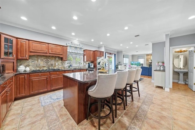 kitchen with a kitchen breakfast bar, tasteful backsplash, dark stone countertops, a kitchen island, and ornamental molding