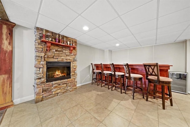 bar featuring a paneled ceiling, a stone fireplace, and tile patterned floors