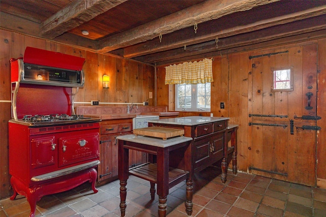 kitchen featuring beamed ceiling, wood walls, and stainless steel gas cooktop