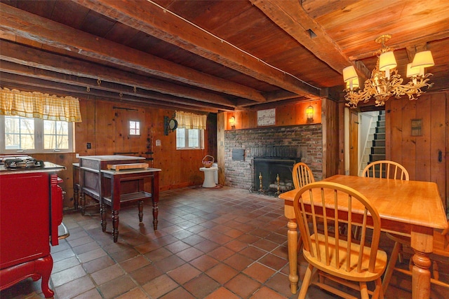 dining room with wooden ceiling, an inviting chandelier, beamed ceiling, wooden walls, and a fireplace